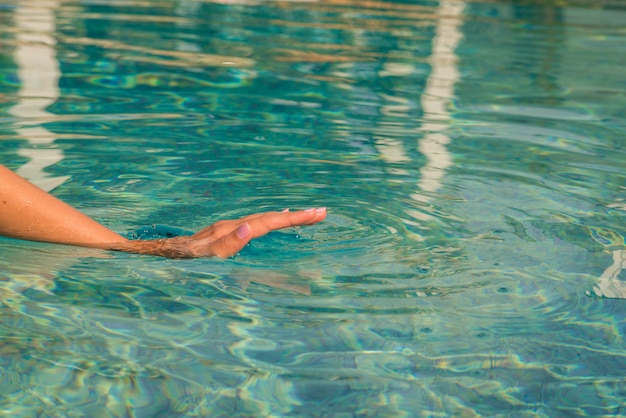 Young woman kneeling by the edge of a swimming pool, touching the calm water with her hand.