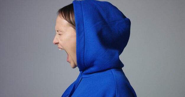 Young woman in large unlabeled bright blue hoodie screams and acts scared and angry showing stress