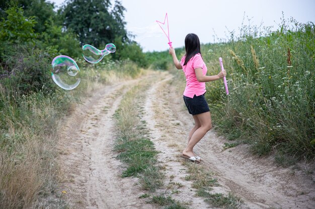 A young woman launches huge soap bubbles in the background beautiful nature, back view.