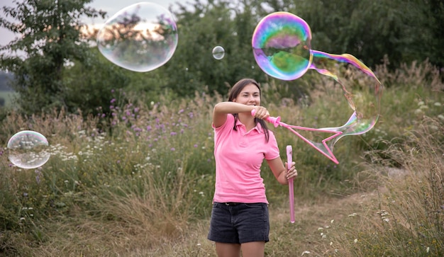 Free Photo a young woman launches large colored soap bubbles among the grass in nature.