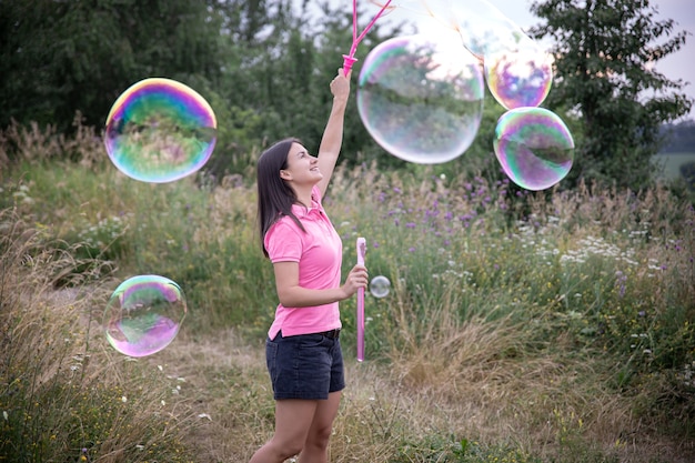 A young woman launches large colored soap bubbles among the grass in nature.