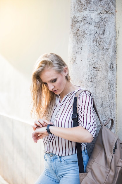 Free Photo young woman leaning against wall looking at time on wrist watch