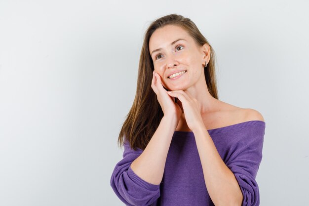 Young woman leaning cheek on palm in violet shirt and looking hopeful. front view.