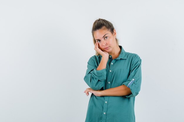 Young woman leaning cheek on palm while thinking about something in green blouse and looking pensive