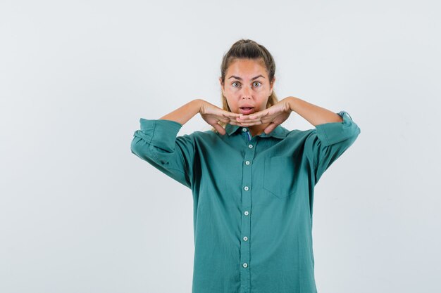 Young woman leaning at her combined hands in blue shirt and looking surprised