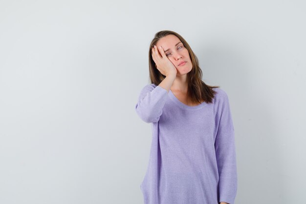 Young woman leaning at her hand in lilac blouse and looking bored. front view. space for text