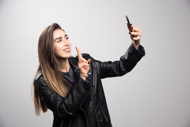 Young woman in leather jacket taking selfie with her cell phone