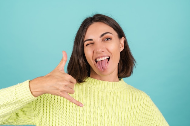 Young woman in light green sweater smiling shows phone gesture