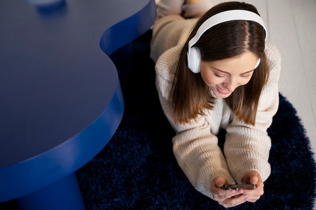 Free Photo young woman listening to music using her smartphone while laying on the floor