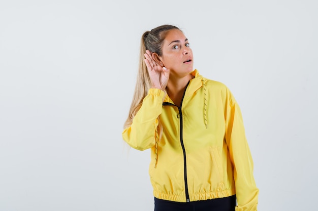 Young woman listening in yellow raincoat and looking concentrated