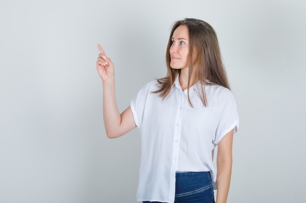 Young woman looking away with finger up in white t-shirt, jeans and looking glad