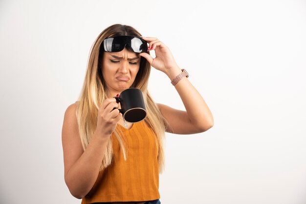 Young woman looking on black cup and wearing goggles.