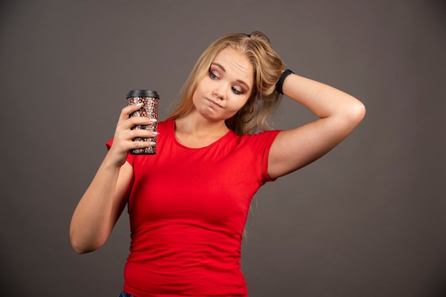 Free photo young woman looking at cup of coffee on black wall.