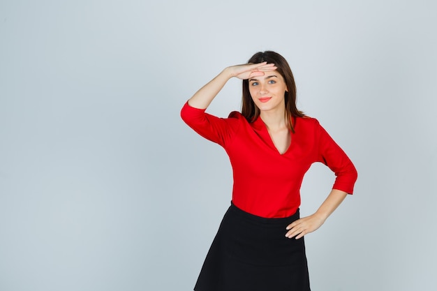 Young woman looking far away with hand over head, holding hand on hip in red blouse