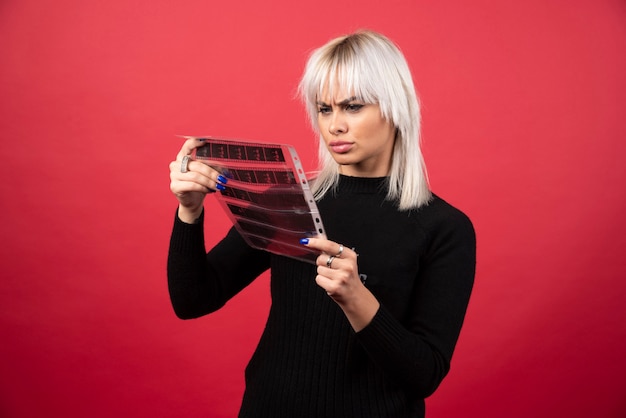 Free photo young woman looking on a photo tape on a red background . high quality photo