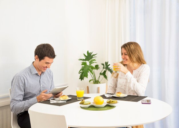 Young woman looking at smiling man using digital tablet at breakfast table