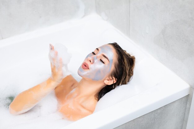 Young woman lying in bathtub with a sheet mask on her face