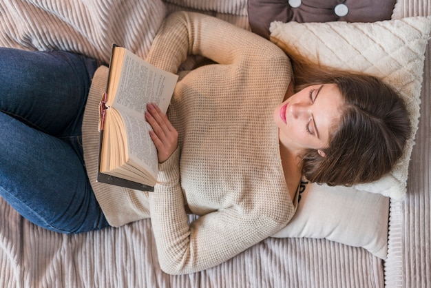 Young woman lying on bed reading book