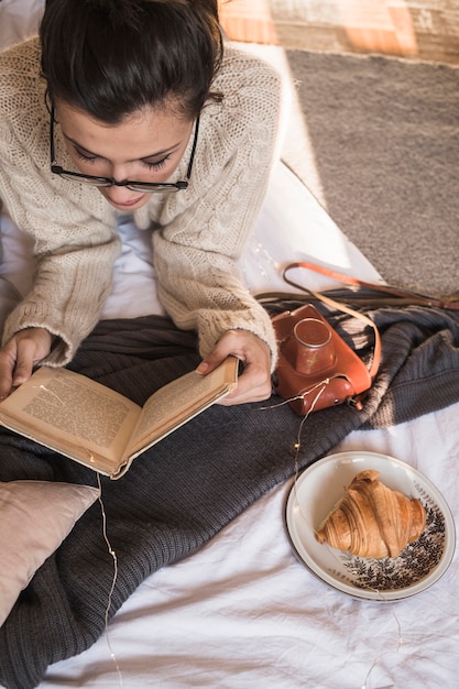 Free photo young woman lying on blanket and reading book