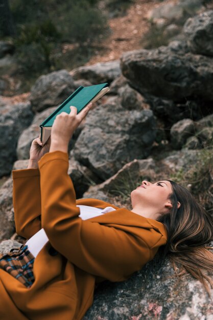 Young woman lying on rock reading the book