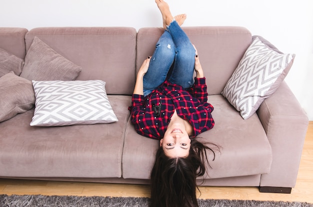 Free photo young woman lying on sofa with her legs up at home