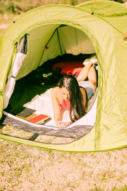 Young woman lying in tent with smartphone