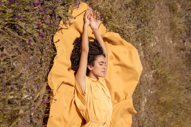 Free photo young woman lying on yellow cloth in nature