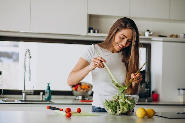 Free photo young woman making salad at the kitchen