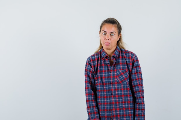 Young woman making squint for fun in checked shirt and looking amused.  front view.