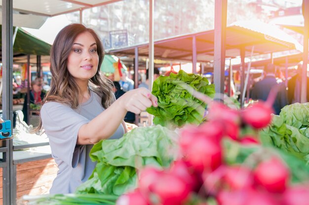 Young woman on the market. Happy young brunette  picking some vegetables. Portrait of beautiful young woman choosing green leafy vegetables