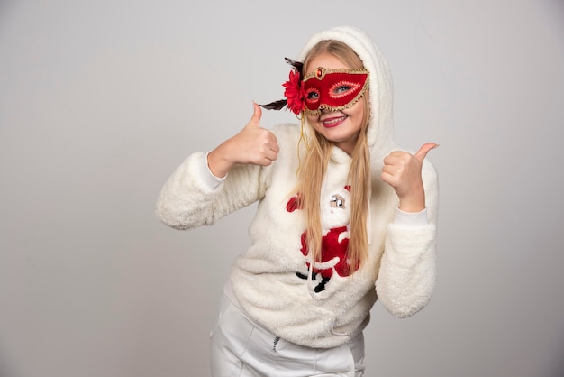 Free photo young woman in masquerade mask giving thumbs up.