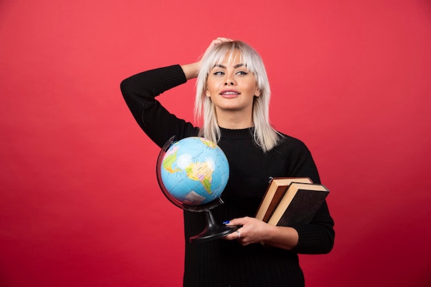 Free Photo young woman model posing with a books and a earth globe on a red wall. 