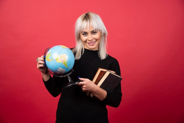 Young woman model posing with a books and a Earth globe on a red wall. 