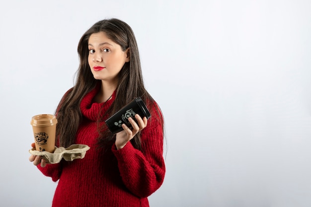 A young woman model in red sweater holding two cups of coffee