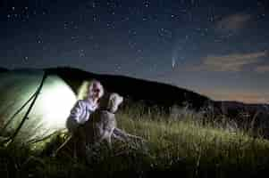 Free photo young woman in the mountains observing beautiful starry night and a comet