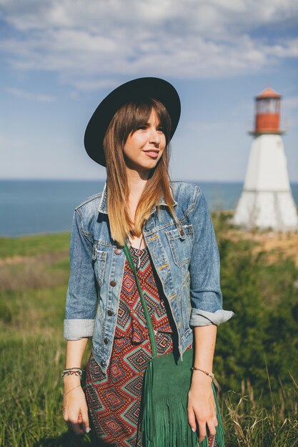 Young woman in nature, lighthouse, bohemian outfit, denim jacket, black hat, smiling, happy, summer, stylish accessories