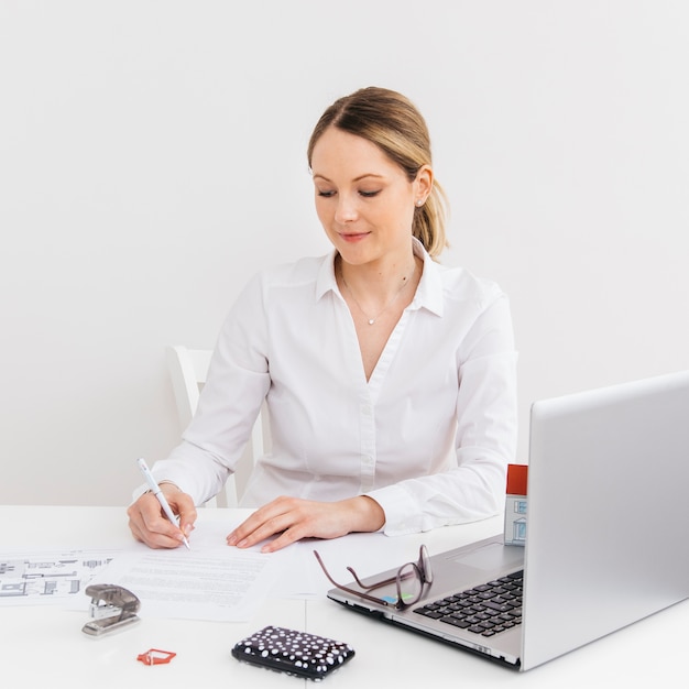 Free photo young woman in office doing paperwork in front of laptop