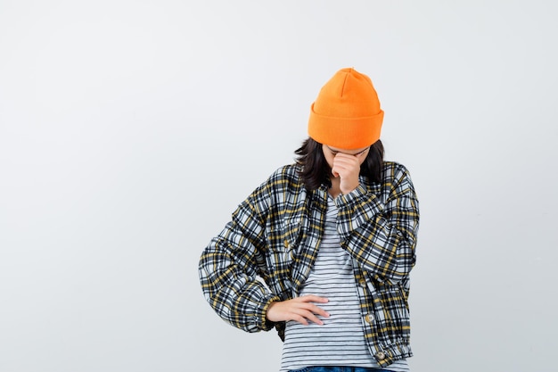 Young woman in orange hat and checkered shirt leaning head on hand and looking upset