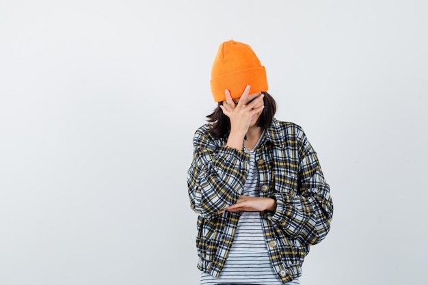 Young woman in orange hat and checkered shirt leaning head with hand looking happy