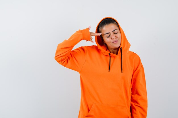 Young woman in orange hoodie pointing at herself with index finger and looking serious 