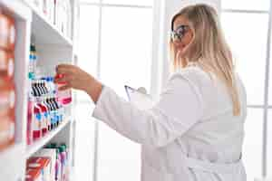 Free photo young woman pharmacist reading document holding medication bottle at pharmacy