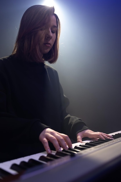 Young woman pianist plays the keys in a dark room with haze