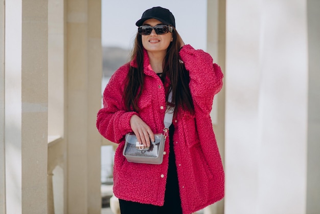 Free photo young woman in pink coat standing in the street