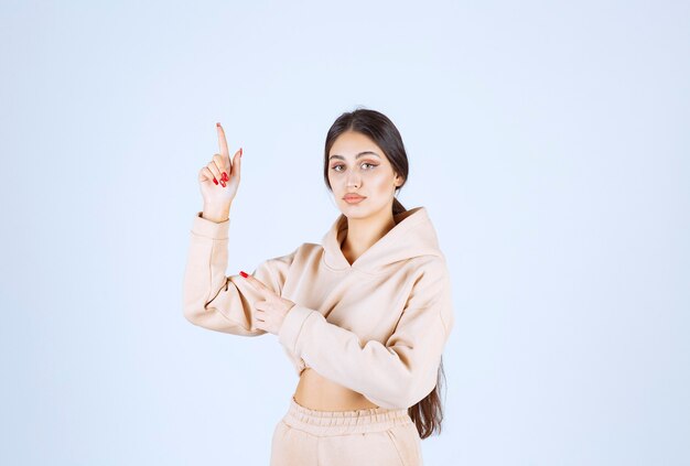 Young woman in a pink hoodie pointing somewhere above