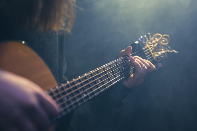 Young woman playing acoustic guitar in a dark room with haze