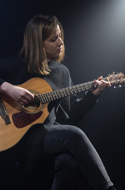 Young woman playing acoustic guitar in a dark room with haze