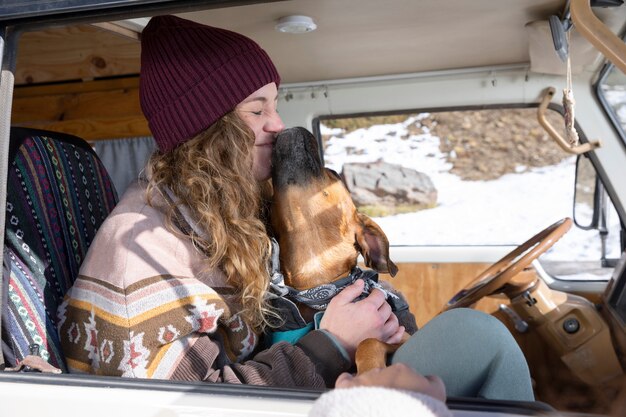 Free photo young woman playing with her dog inside camper van during winter trip