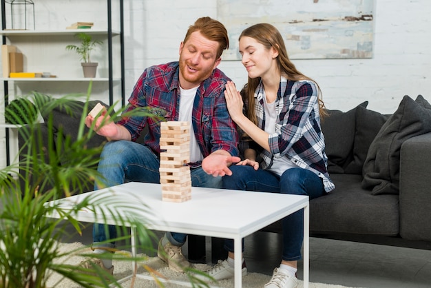 Free photo young woman pleasing her boyfriend after removing the wooden block from tower at home