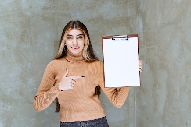 Free Photo young woman pointing at an empty notepad on a stone 