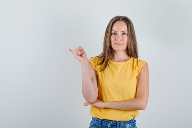 Young woman pointing finger away in t-shirt, shorts and looking glad